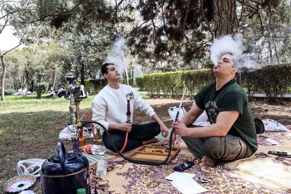 Photo by - / AFP. Iranian men smoke waterpipes as they sit in Tehran's Mellat park on April 2, 2026, during "Sizdeh Bedar" (Nature Day), the 13th day after the Nowruz Persian New Year, when people traditionally picnic outdoors with family and friends.