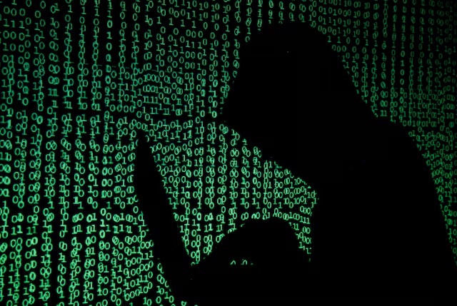 A hooded man holds a laptop computer as cyber code is projected on him in this illustration picture taken on May 13, 2017. REUTERS/Kacper Pempel/Illustration/File Photo