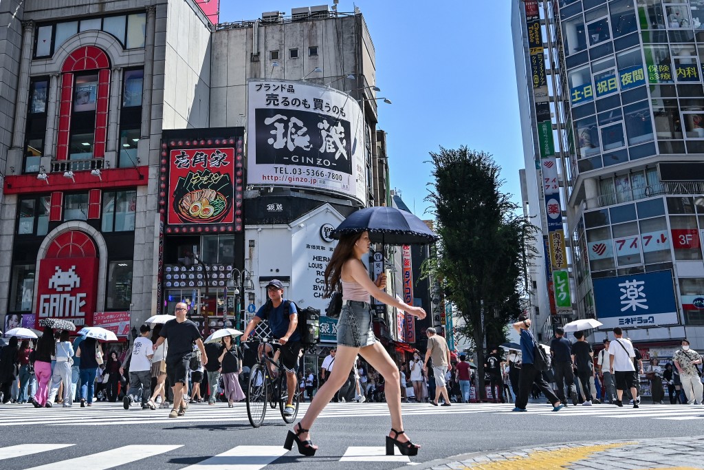 A woman carries an umbrella to shelter from the sun as pedestrians cross a street in the Kabukicho entertainment area of Shinjuku in central Tokyo. (AFP)