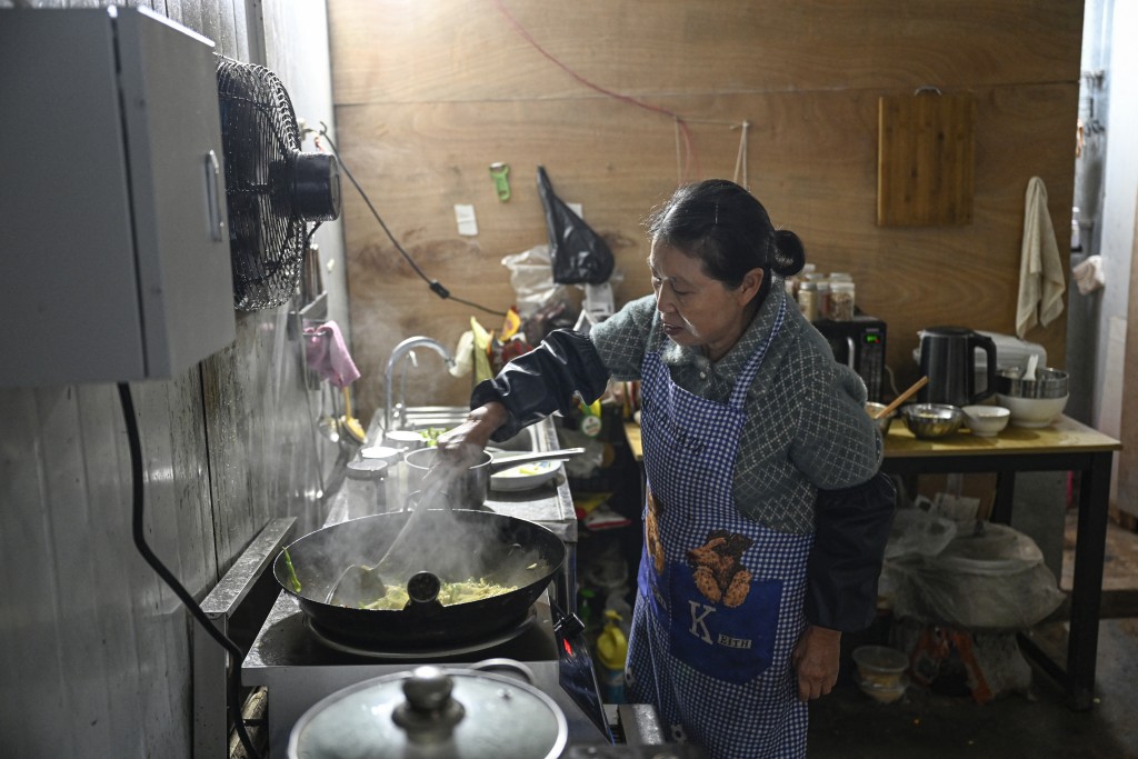 Photo by JADE GAO / AFP  This photo taken on December 16, 2025 shows Wu Dimei cooking for her son Li Xia, who has Duchenne muscular dystrophy, at the kitchen in southwestern China's Chongqing municipality.