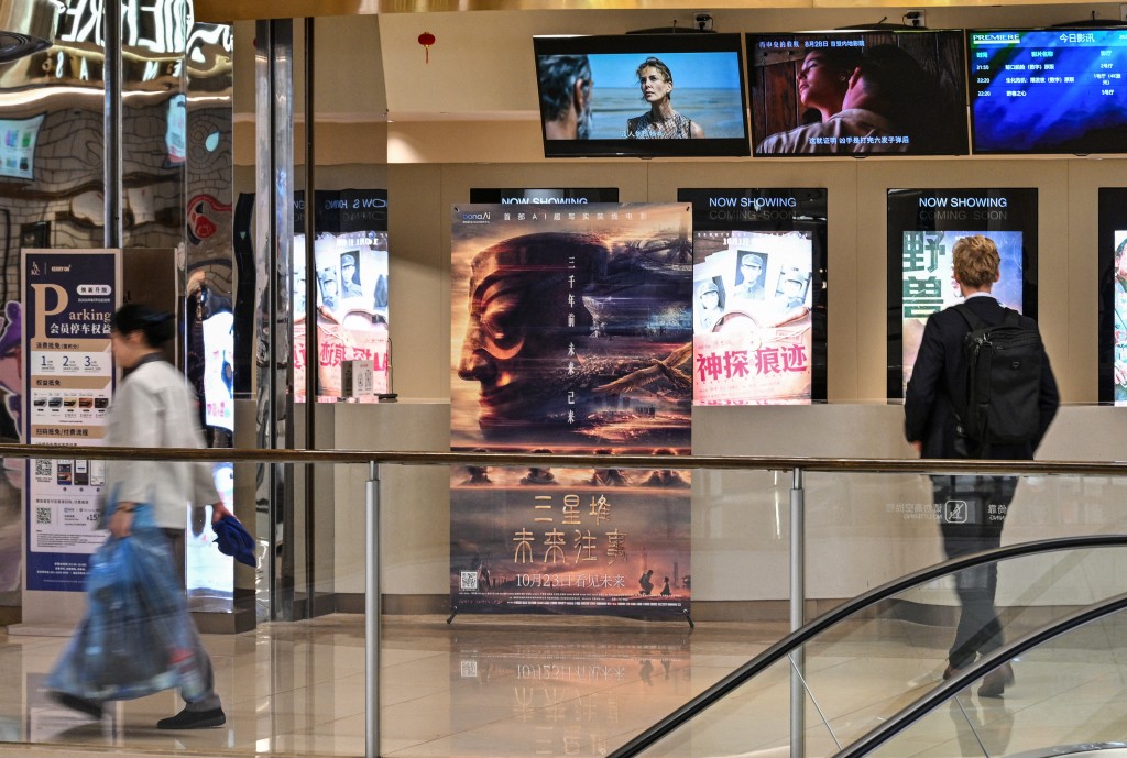 People walk next to a poster of the AI-generated movie "Sanxingdui: Future Memories" in a cinema in the Jing'an Temple district in Shanghai on October 22, 2026. (Photo by Hector RETAMAL / AFP)
