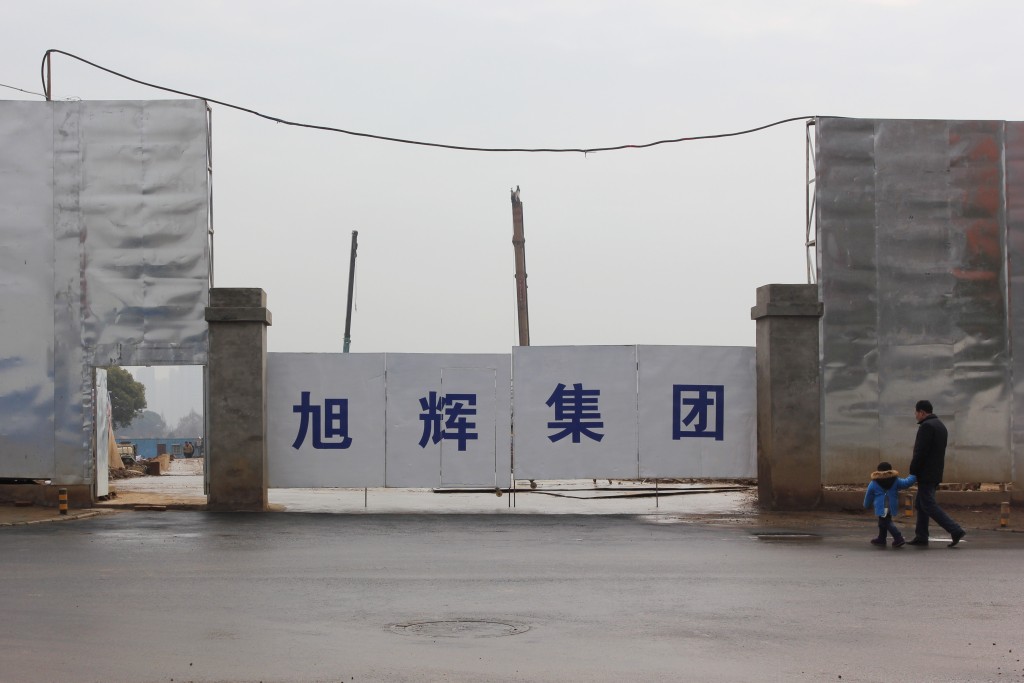 A man and a child walk by a construction site under property developer CIFI Holdings in Wuhan, Hubei province, China February 4, 2016. Reuters