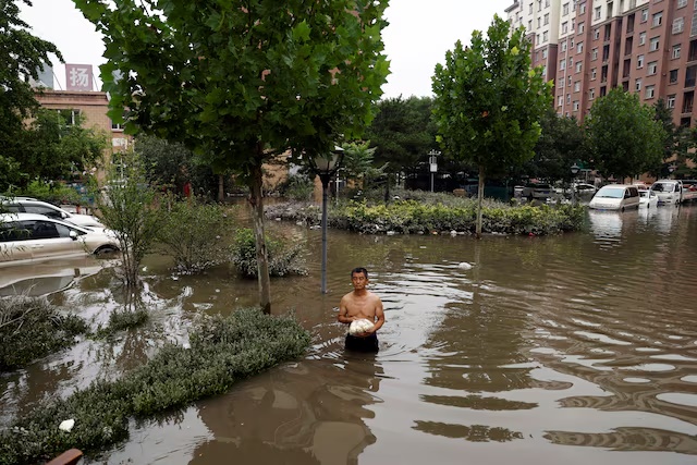 A man holding a bag of food wades through floodwaters after the rains and floods brought by remnants of Typhoon Doksuri, in Zhuozhou, Hebei province, China August 3, 2023. REUTERS/Tingshu Wang/File Photo