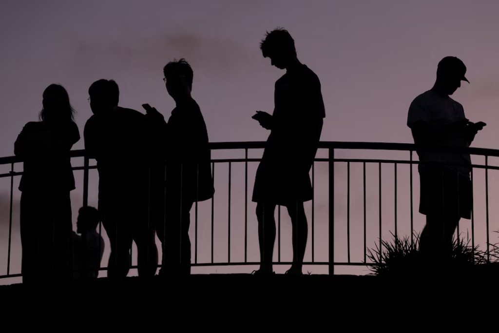 People use their mobile phones at dusk in Brisbane, Australia, December 8, 2025. REUTERS/Hollie Adams 