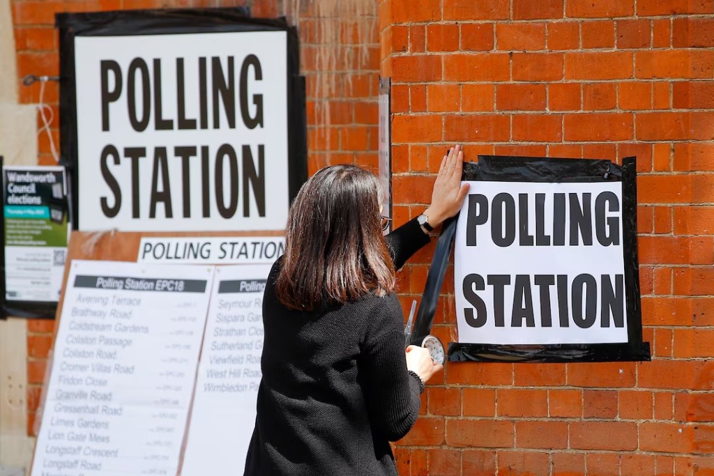 A woman attaches a sign on the wall of a polling station, during the local elections in London, Britain May 5, 2022. REUTERS/Peter Nicholls/File Photo 