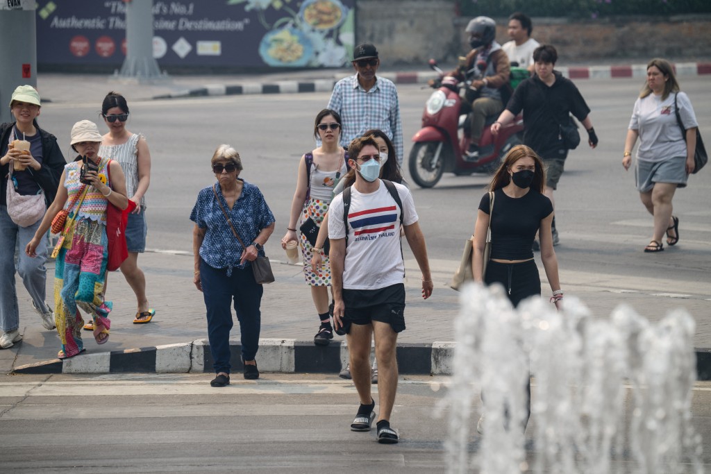 Photo by ANTHONY WALLACE / AFP. Pedestrians walk across a road on a heavily polluted day in Chiang Mai on April 2, 2026.