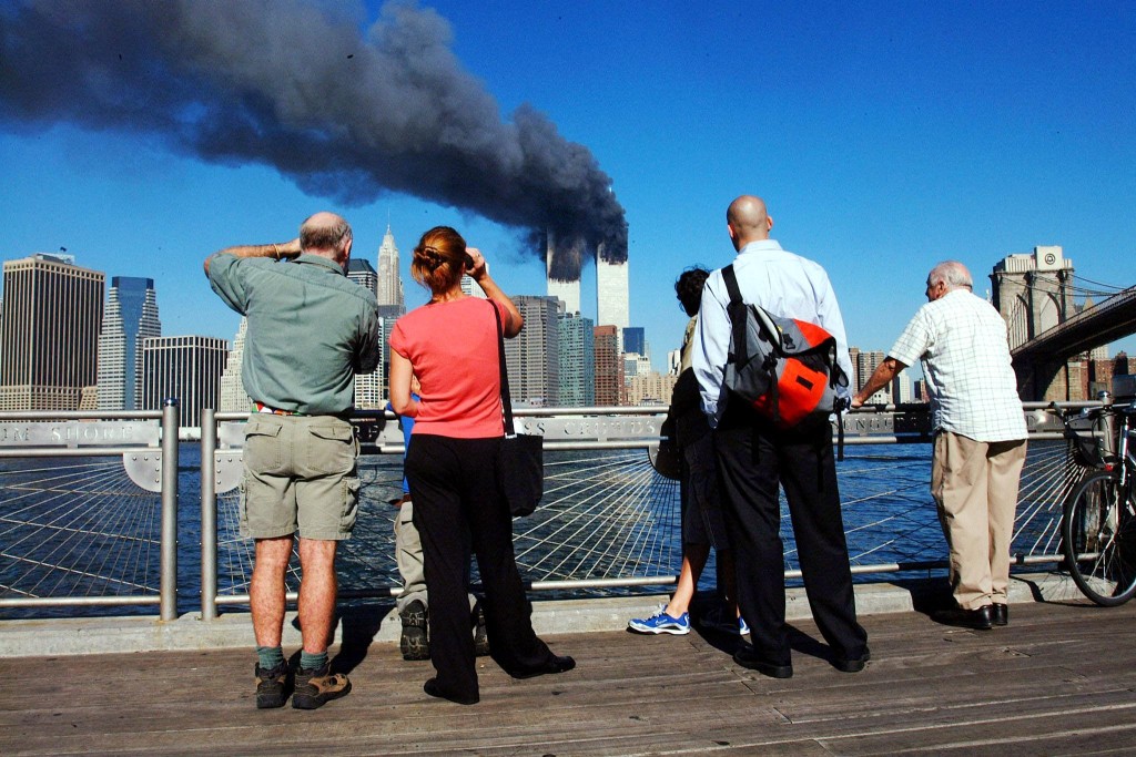 Photo by HENNY RAY ABRAMS / AFP In this file photo pedestrians standing on the Brooklyn waterfront look across the East River towards the burning twin towers of the World Trade Center in lower Manhattan, New York on September 11, 2001.