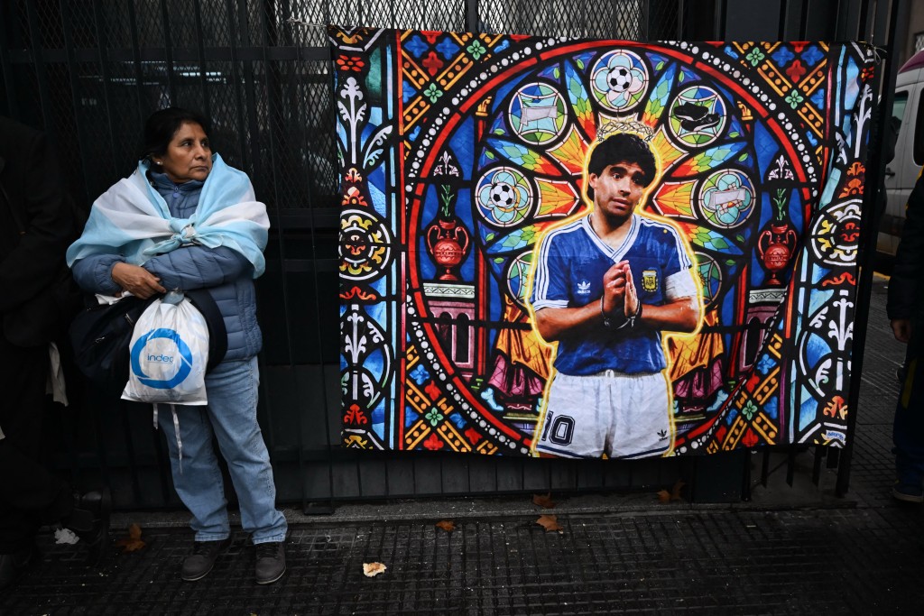 A woman stands next to a banner depicting late Argentine football legend Diego Maradona outside the National Congress in Buenos Aires on August 6, 2026, as senators debate a bill on the inviolability of private property. (Photo by Luis ROBAYO / AFP)