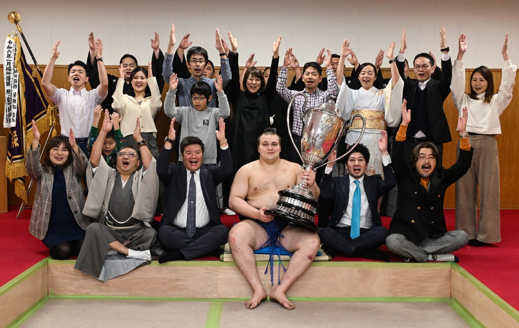 Ukrainian sumo wrestler Danylo Yavhusishyn (front C), also known by his Japanese ring name Aonishiki Arata poses with the trophy to celebrate after winning the Grand Sumo Tournament in Fukuoka on November 23, 2025. (Photo by JIJI PRESS / AFP) / JAPAN OUT