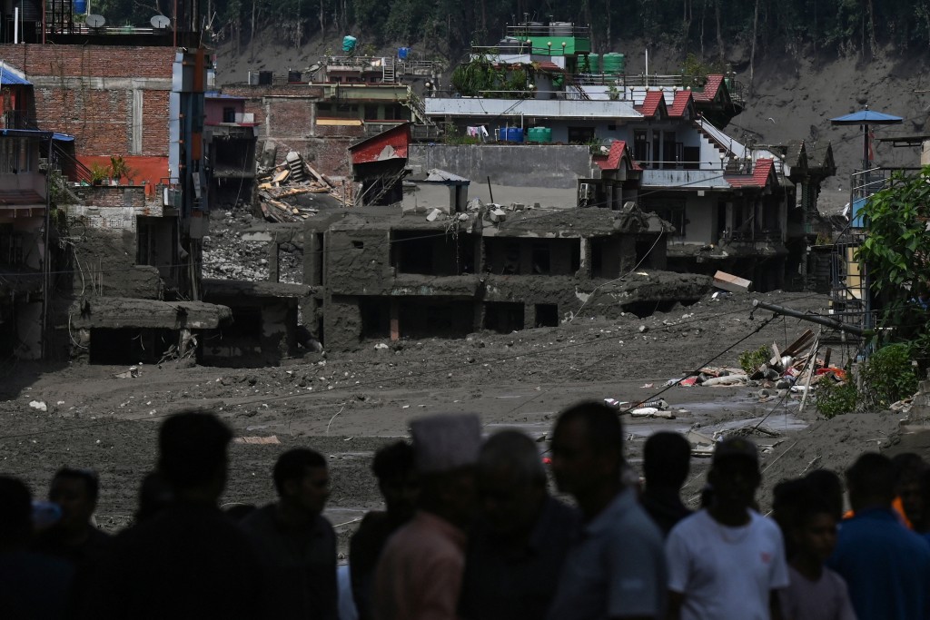 Photo by PRAKASH MATHEMA / AFP  Residents look at buildings submerged by mud following flash floods and a landslide disaster in Trishuli Bazar, in Nepal's Nuwakot district on August 26, 2026.
