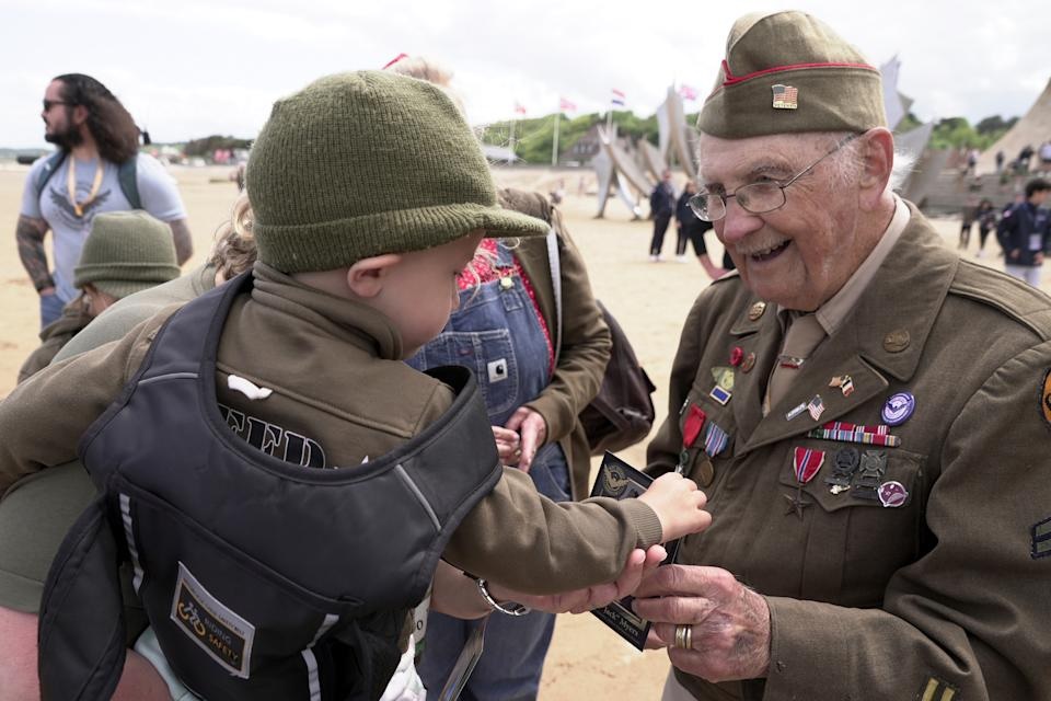 World War II veteran Wilbur "Jack" Myers, a 101-year-old who fought in the U.S. Army's 692nd Tank Destroyer Battalion, hands a souvenir postcard of himself to Ryan, a young French boy, on Monday, June 2, 2025, at Omaha beach, which was one of the D-D-day invasion spots on June 6, 1944. (AP Photo/John Leicester)