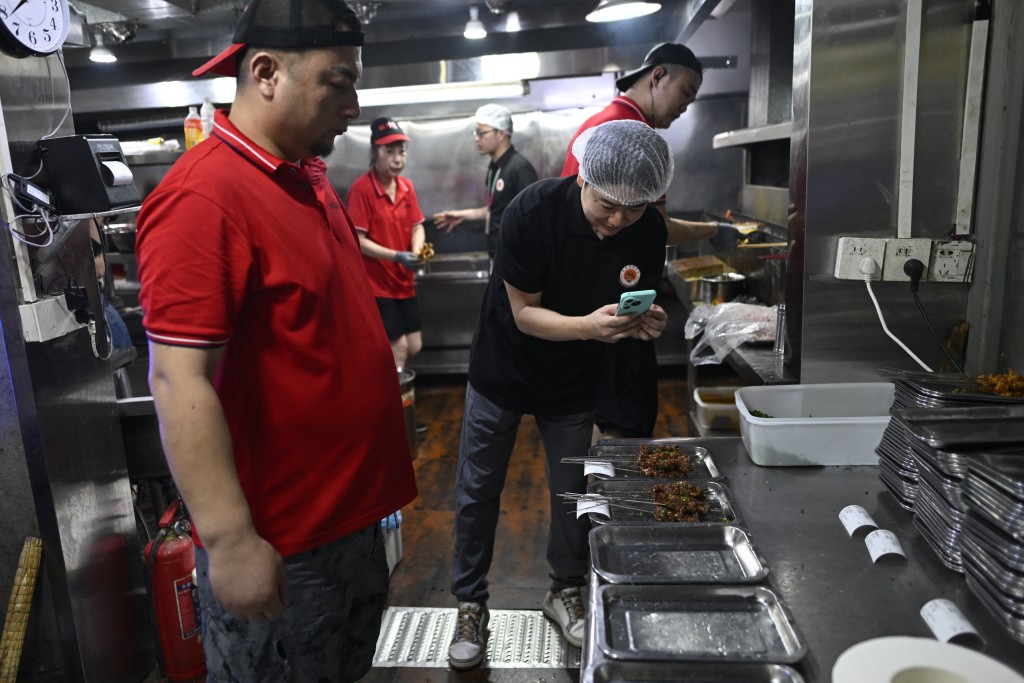 Photo by WANG ZHAO / AFP  This picture taken on June 15, 2026 shows a trainee using a mobile phone to take pictures during a visit of a barbecue restaurant in Yueyang, in southern China's Hunan province.