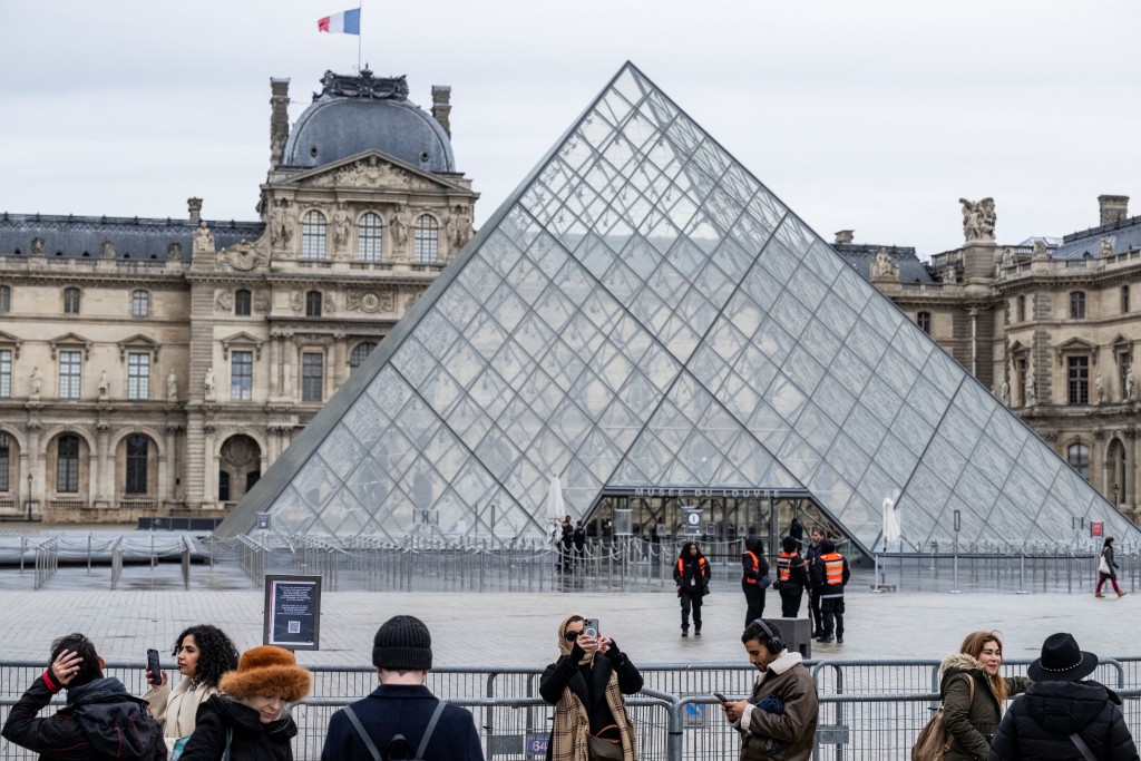 Photo by MARTIN LELIEVRE / AFP  Tourists stand behind barriers blocking the access to the Louvre main courtyard, La Cour Napoleon, with the Louvre Pyramid, designed by Chinese-US architect Ieoh Ming Pei, as the Louvre Museum is closed due a strike, in Paris, on January 12, 2026.