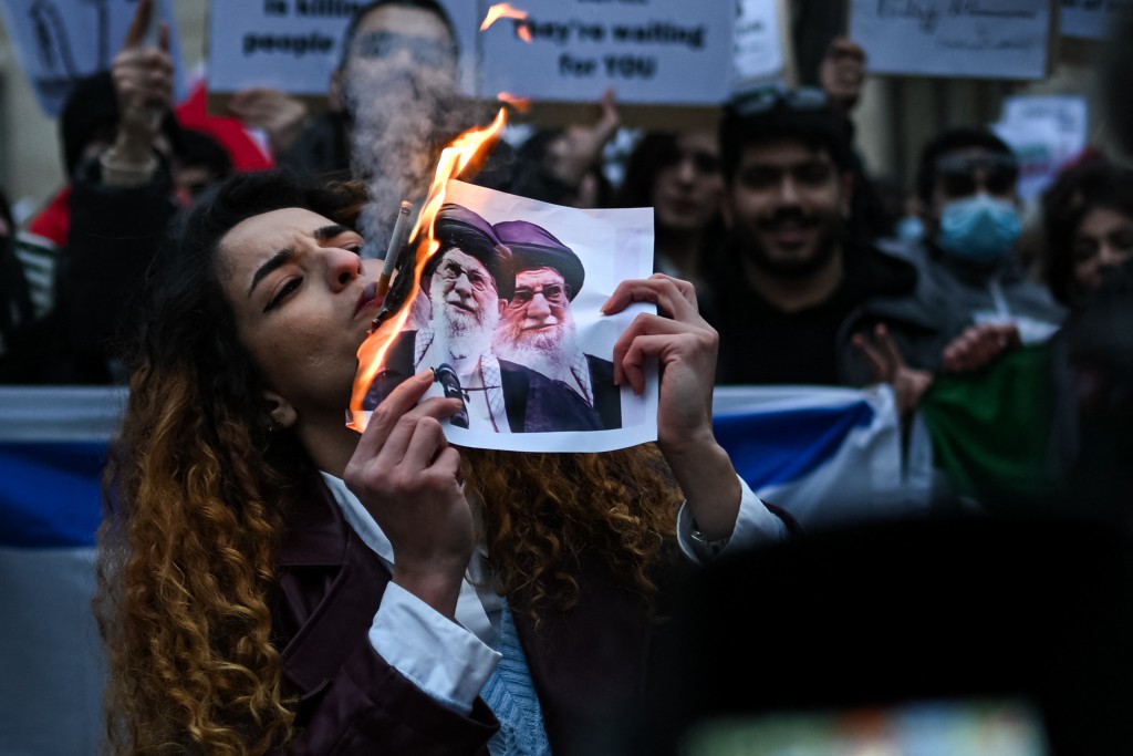 TOPSHOT - An anti-Iranian regime protester lights a cigarette with a lit paper depicting Ali Khamenei, Supreme Leader of Iran during a gathering outside the US Consulate in Milan, on January 13, 2026. (Photo by Piero CRUCIATTI / AFP)
