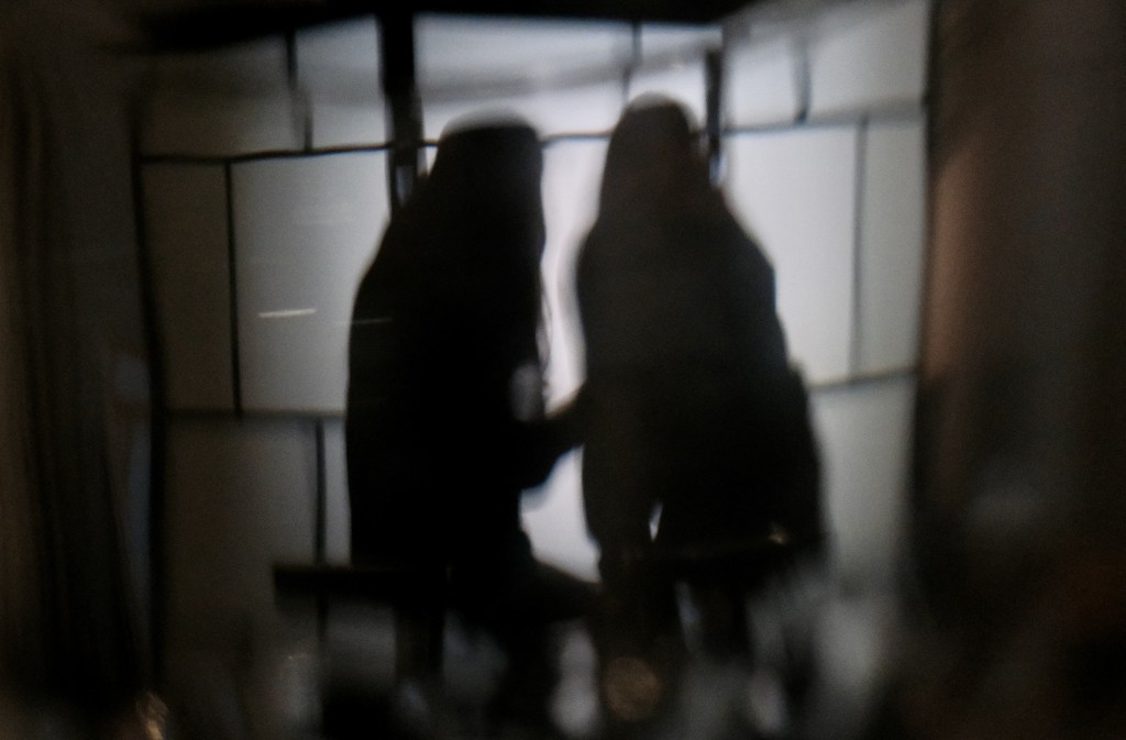 This photo taken through glass on July 29, 2025 shows University of Hong Kong (HKU) students "B" and "C" scrolling through their phones in Hong Kong. (Photo by Tommy WANG / AFP)