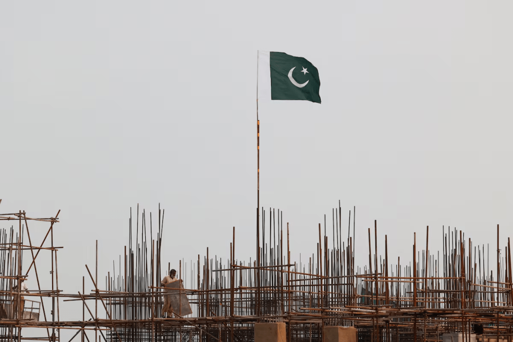 A Pakistani flag flutters over iron scaffoldings as a labourer works at a construction site on the eve of Pakistan's Independence Day celebrations, in Lahore, Pakistan August 13, 2025. REUTERS/Akhtar Soomro/File Photo 