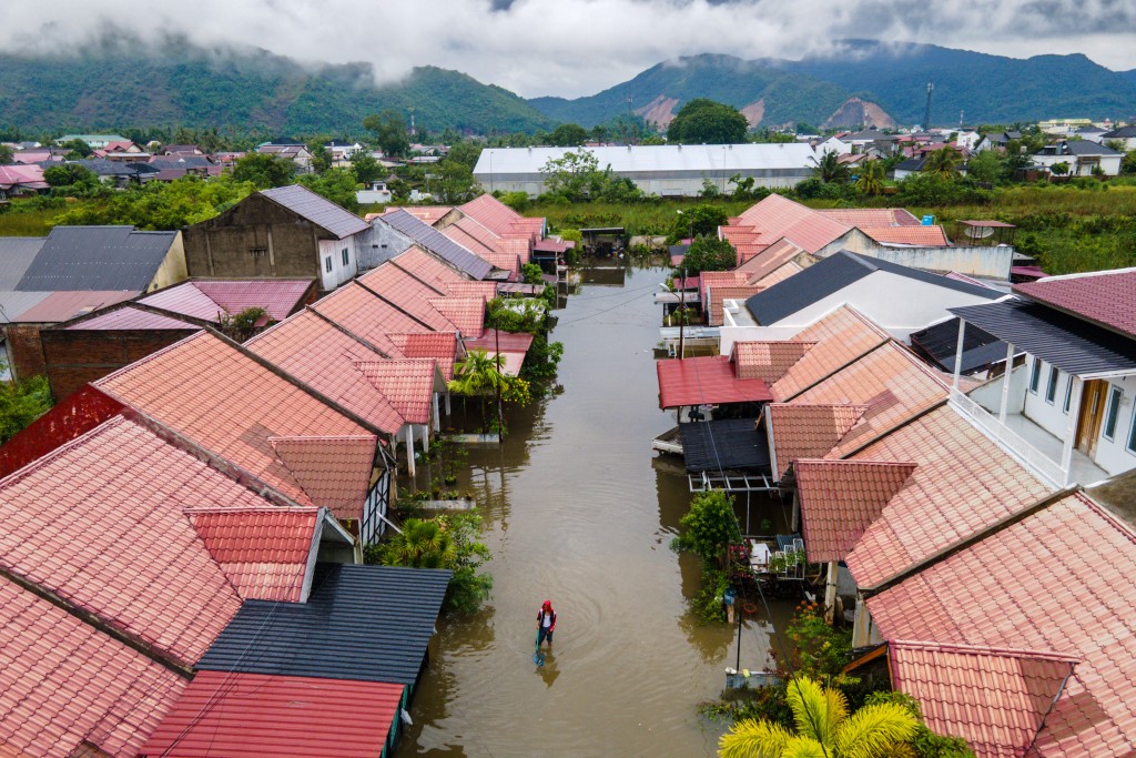 This aerial picture shows a man wading through the floodwaters following heavy rain at a residential area of Darul Imarah on the outskirts of Banda Aceh on November 27, 2025. (Photo by CHAIDEER MAHYUDDIN / AFP)