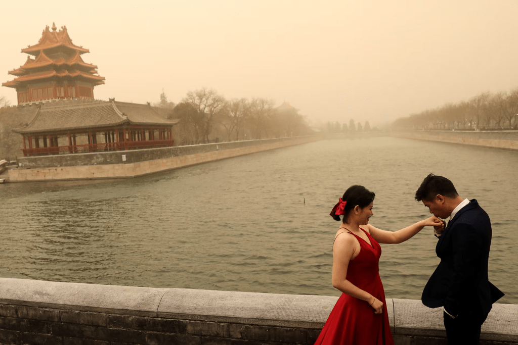 A couple react during their wedding photoshoot near the Forbidden City, as the city is hit by sandstorm, in Beijing, China March 15, 2021. REUTERS/Tingshu Wang
