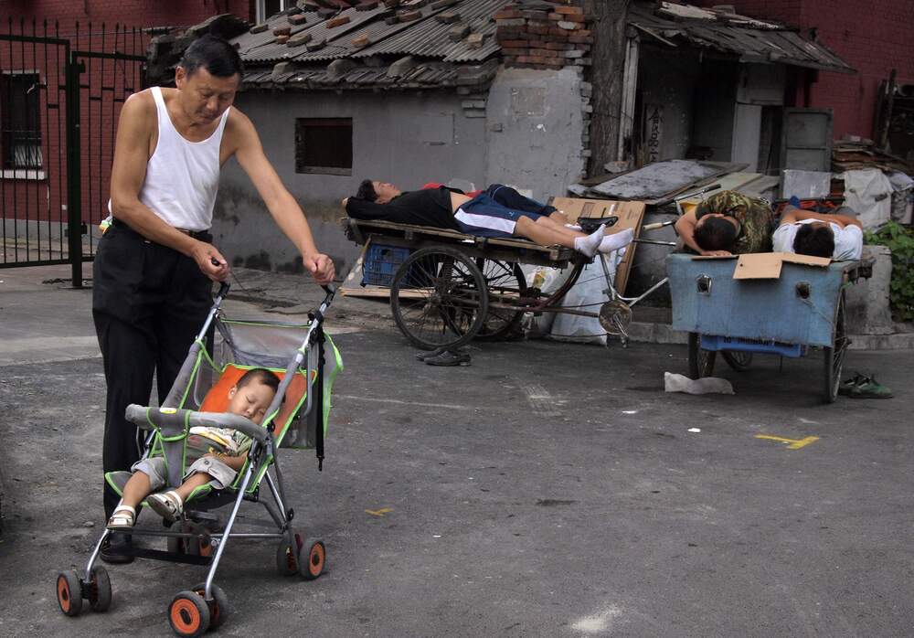 An elderly man pushes a napping child past Chinese men sleeping on carts on the streets of Beijing, China. (AP) An elderly man pushes a napping child past Chinese men sleeping on carts on the streets of Beijing, China. (AP)