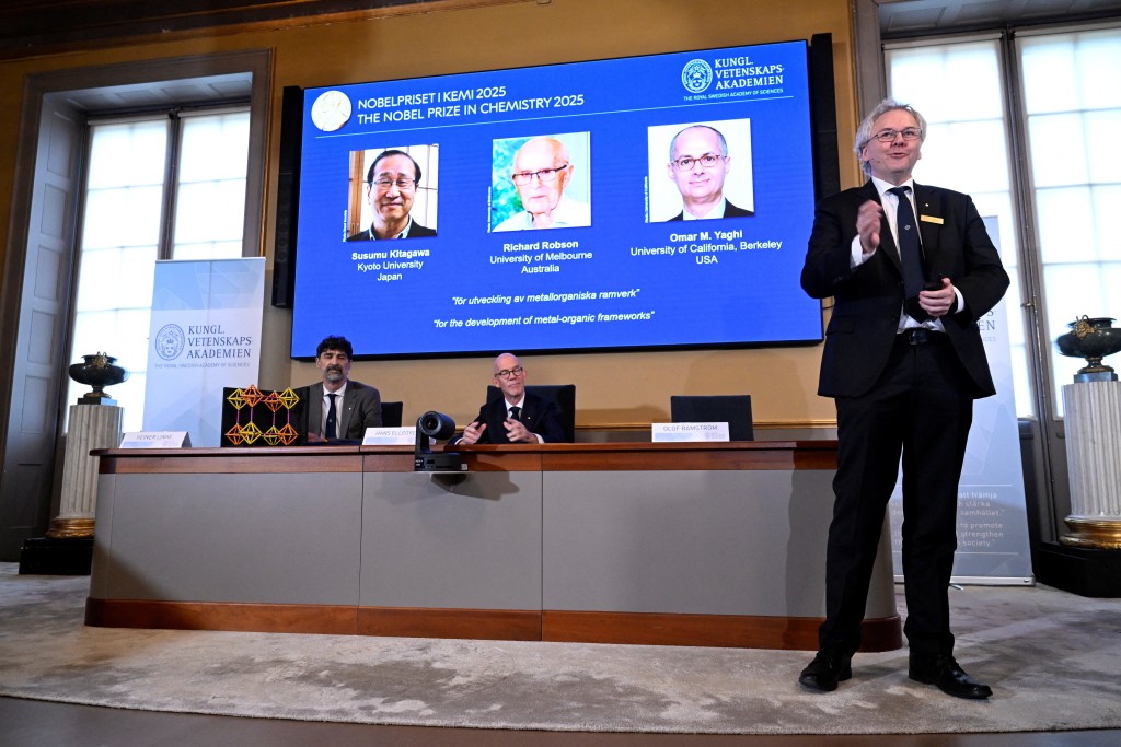 A screen displays the 2025 Nobel Prize laureates in Chemistry, Susumu Kitagawa (Kyoto University, Japan), Richard Robson (University of Melbourne, Australia), and Omar M. Yaghi (University of California, Berkeley, U.S.) (Reuters)