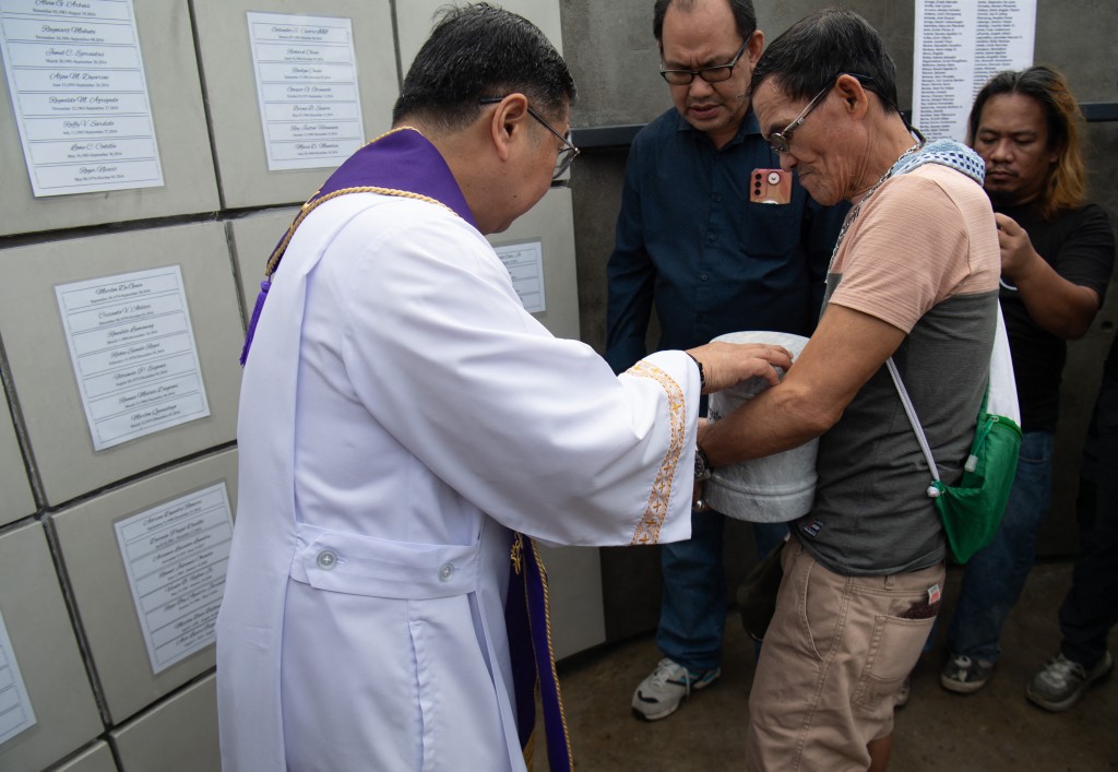 Photo by TED ALJIBE / AFP  A relative of one of the victims of extrajudicial killings of former Philippine president Rodrigo Duterte's drug war, hands over the urn of his son to Father Flavie Villanueva during the inurnment rites at the "Dambana ng Paghilom" (Shrine of Healing)at a cemetery in Caloocan city, suburban Manila on February 20, 2026.