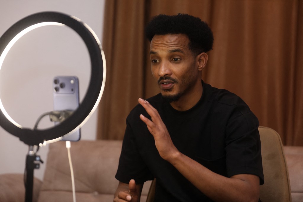 Photo by HASSAN ALI ELMI / AFP Mahad Maxamud interacts with followers as he goes live on social media in Mogadishu on December 6, 2025.