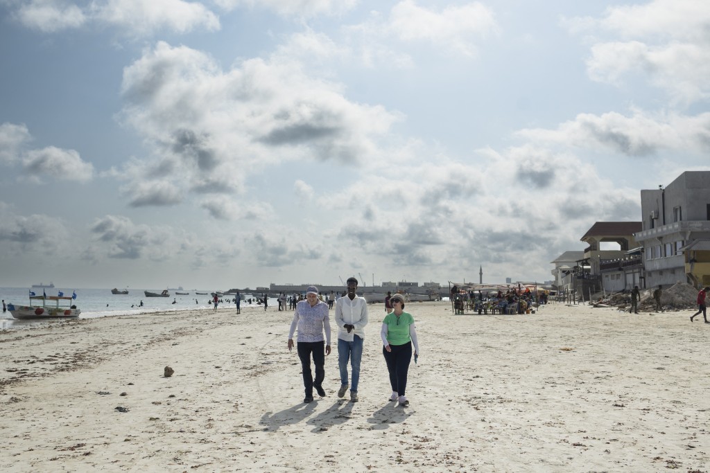 Photo by TONY KARUMBA / AFP  US tourists Richard (L) and Sheryl (R) walk along with a local tour guide (C) on Lido beach during a guided tour of tourist attractions in Mogadishu on November 10, 2025.
