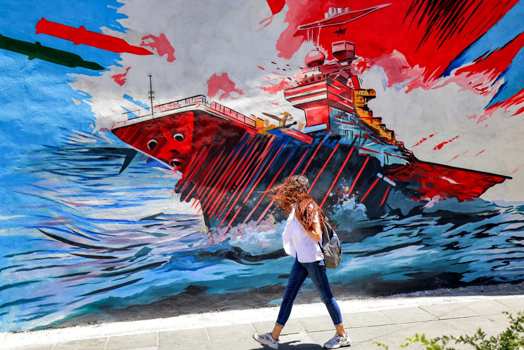 Photo by ATTA KENARE / AFP  A woman walks past an anti-US and anti-Israel mural depicting missiles hitting an aircraft carrier in Tehran on May 26, 2026.