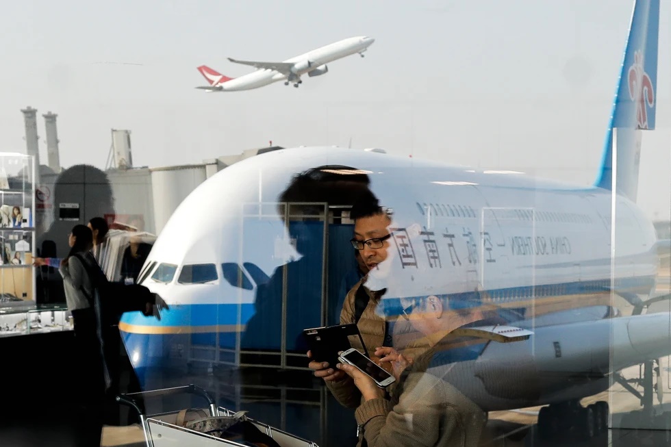Passengers walk past a couple browsing their smartphones near a China Southern Airlines, parked on the tarmac at the Beijing Capital International Airport Saturday, Nov. 19, 2016.(AP Photo/Andy Wong, File)