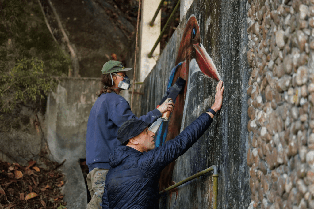 Dominic Johnson-Hill looks at a white-throated kingfisher mural being painted by Rob Aspire near Wang Tong village, Lantau, Hong Kong, Jan. 27, 2025. (AP Photo/May James)