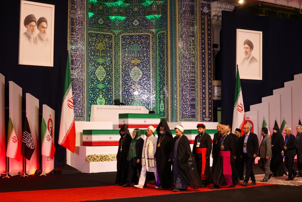 Photo by ATTA KENARE / AFP  Local and foreign officials walk past the coffins of Iran's slain supreme leader Ali Khamenei and his family members after paying their respects at the Grand Mosalla in Tehran on July 3, 2026.