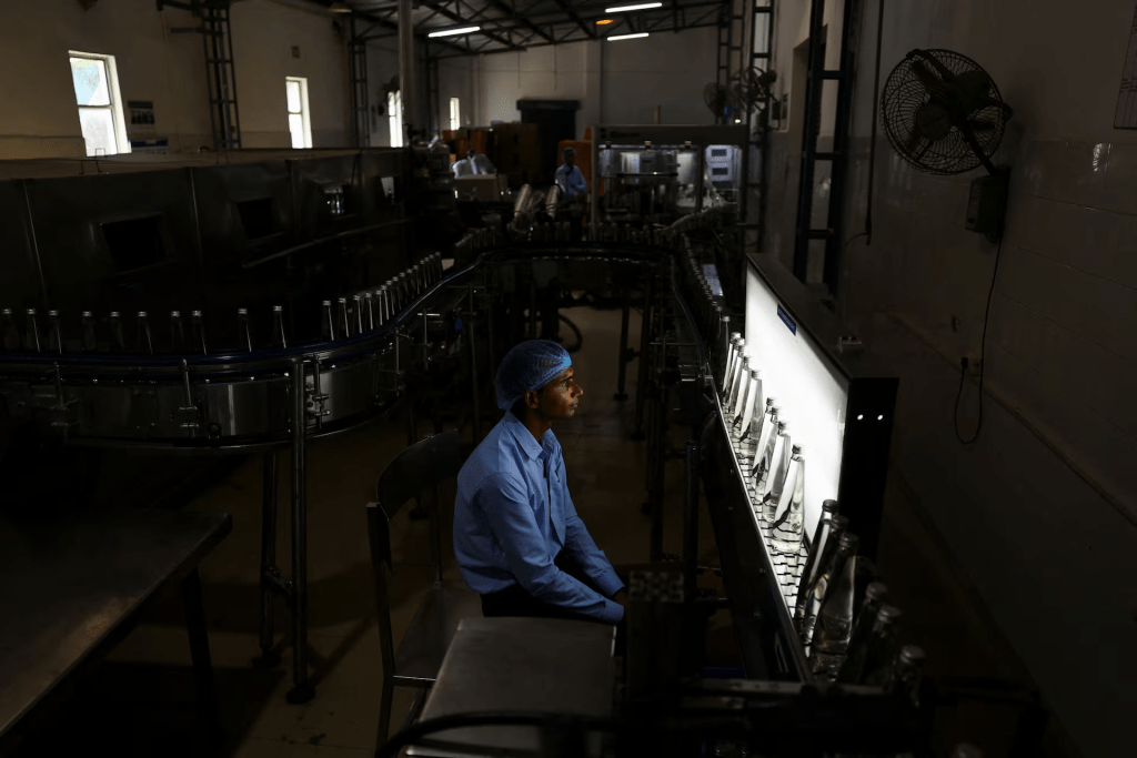 A worker inspects glass bottles filled with water against a bottle inspection light at Tata's Himalayan natural mineral water bottling plant in Dhaula Kuan, Himachal Pradesh, India, October 16, 2025. REUTERS/Anushree Fadnavis 