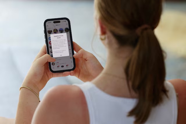 A teenager poses holding a mobile phone displaying a message from TikTok as law banning social media for users under 16 in Australia takes effect, in Sydney, Australia, December 10, 2025. REUTERS/Hollie Adams/File Photo 