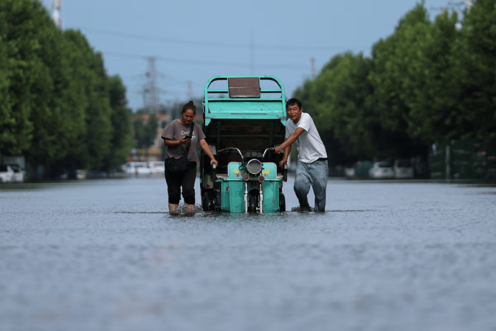 Residents push a vehicle as they wade through a flooded street, following heavy rainfall brought by remnants of Typhoon Dolphin, in Xuchang, Henan province, China August 13, 2026. REUTERS/Tingshu Wang