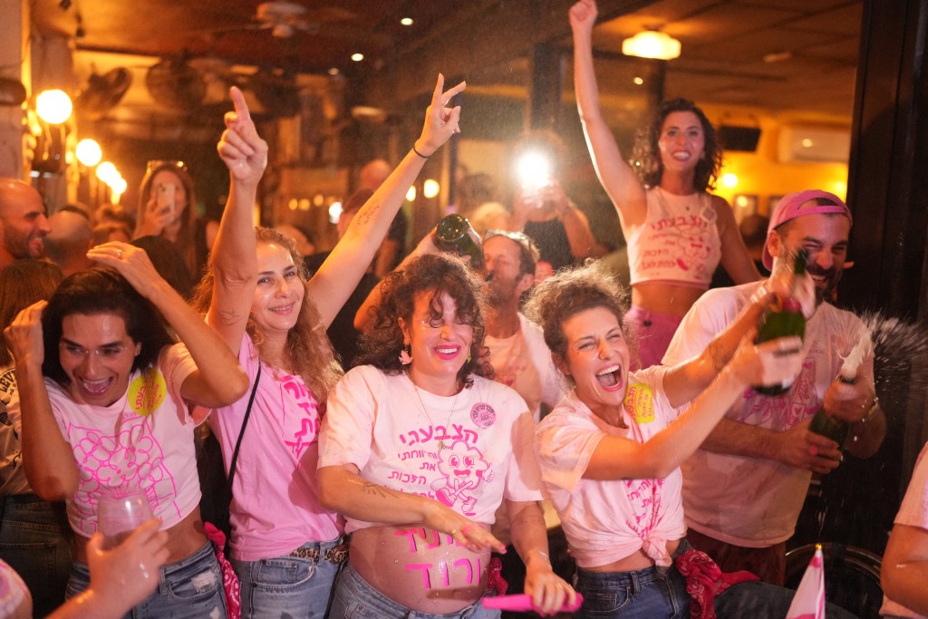 Photo by MAYA LEVIN / AFP Israelis cheer at a bar after the first exit polls were announced, in Tel Aviv on October 27, 2026, during Israel's legislative election.