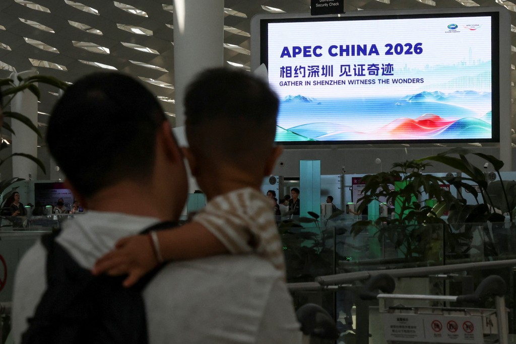 A man holds a child as he stands near a screen showing a promotion for the 33rd Asia-Pacific Economic Cooperation (APEC) Economic Leaders' Meeting, at the Shenzhen Bao'an International Airport, in Shenzhen, Guangdong province, China September 28, 2026. REUTERS/Tingshu Wang