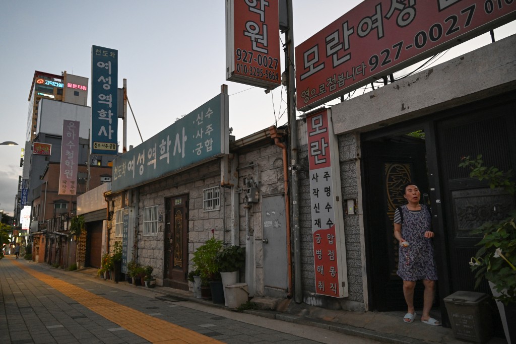 Photo by GREG BAKER / AFP In this photo taken on July 29, 2026, a woman stands below signs advertising fortune telling services in the “Mia-ri fortune-telling village” in Seoul. Photo by GREG BAKER / AFP In this photo taken on July 29, 2026, a woman stands below signs advertising fortune telling services in the “Mia-ri fortune-telling village” in Seoul.