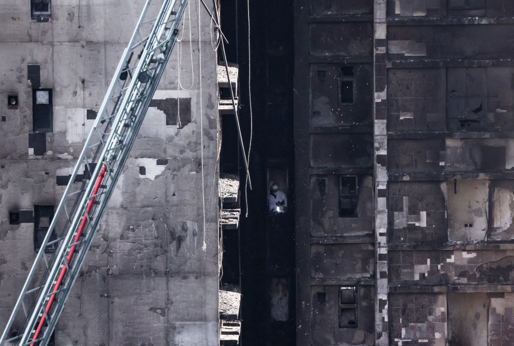 A man wearing personal protective equipment inspects inside one of the buildings of the Wang Fuk Court housing complex after the deadly fire.