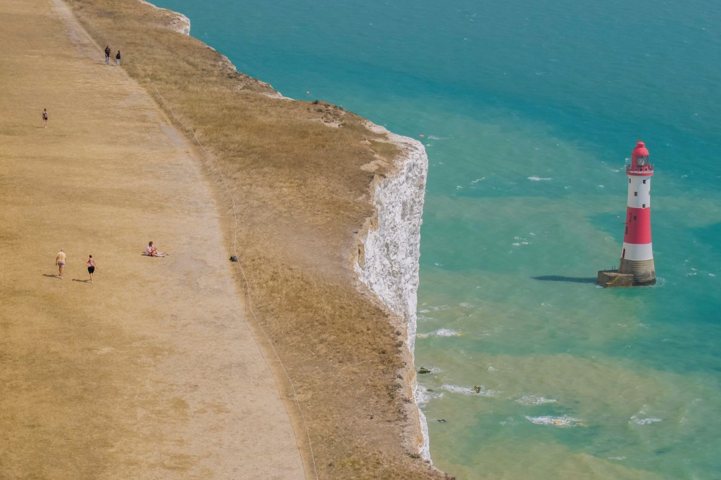 Photo by BROOK MITCHELL / AFP This aerial view shows people walking on bone dry grass, along the cliff-top above the lighthouse at Beachy Head, near Eastbourne on the south coast of England on August 4, 2026.