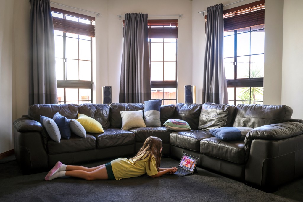 Photo by DAVID GRAY / AFP  This photo taken on October 30, 2025 shows 10-year-old Bianca Navarro lying on the floor as she watches a show on YouTube at her home in western Sydney.