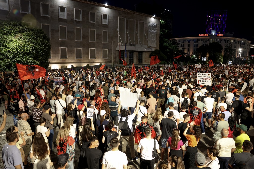 Photo by ADNAN BECI / AFP. Protestors hold placards and Albanian national flags as they gather in front of Albania's Prime Minister's Office during a demonstration against a luxury resort development near a protected natural area, in Tirana on June 19, 2026.