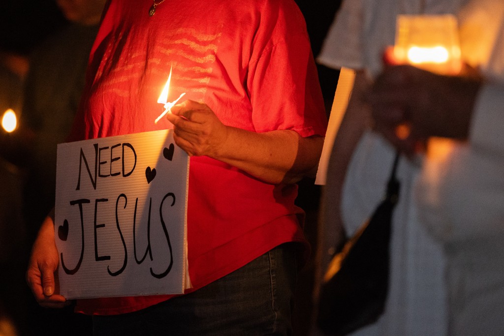 A person holds a sign reading "Need Jesus" and a candle during a candlelight vigil for right-wing activist Charlie Kirk at a makeshift memorial at Memorial Park in Provo, Utah, on September 12, 2025, after he was shot during a public event at Utah Valley University. (Photo by Melissa MAJCHRZAK / AFP)
