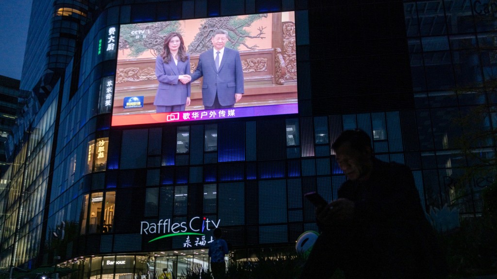 A man uses his smartphone as a giant screen broadcasts news showing Chinese President Xi Jinping shaking hands with Cheng Li-wun, chairperson of the Kuomintang (KMT), Taiwan's largest opposition party at the Great Hall of the People in Beijing, China, April 10, 2026. (Reuters)