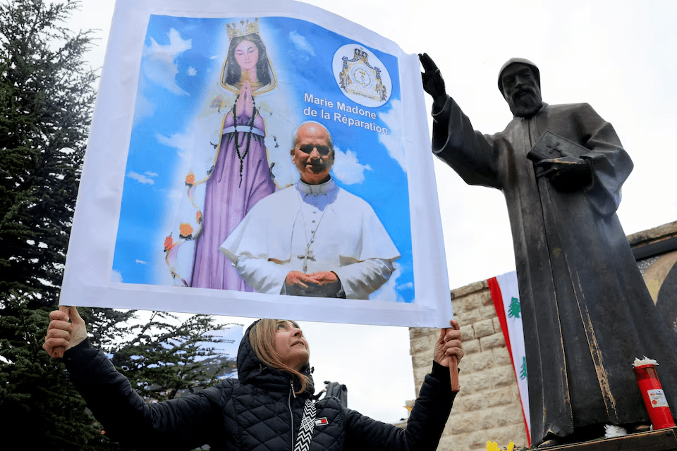  A woman holds up a placard with the images of Pope Leo XIV and "Mary, Madonna of Reparation" next to a statue of St Charbel on the day Pope Leo XIV visits the Monastery of Saint Maroun , in Annaya, Lebanon December 1, 2025. REUTERS/Mohamed Azakir
