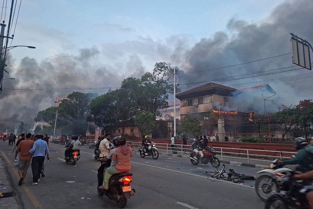 Commuters ride past the burning Supreme Court building, set ablaze by protesters in Kathmandu on September 9, 2025, a day after a police crackdown on demonstrations over social media prohibitions and corruption by the government. (AFP)
