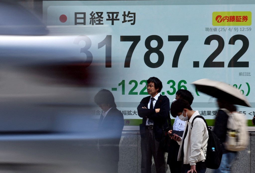 Passersby stand in front of an electronic screen displaying Japan's Nikkei share average outside a brokerage in Tokyo, Japan April 9, 2025. REUTERS