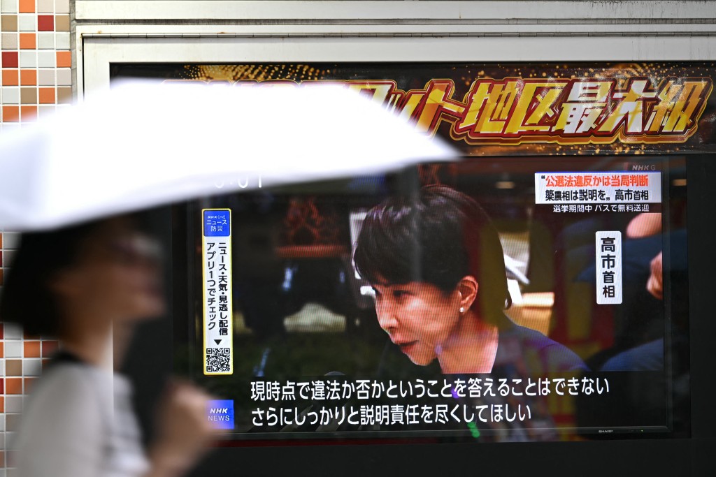 Photo by RIE KIKUCHI / AFP  A woman walks past a screen showing Japan's Prime Minister Sanae Takaichi speaking at a House of Representatives meeting at the National Diet building in Tokyo on October 14, 2026