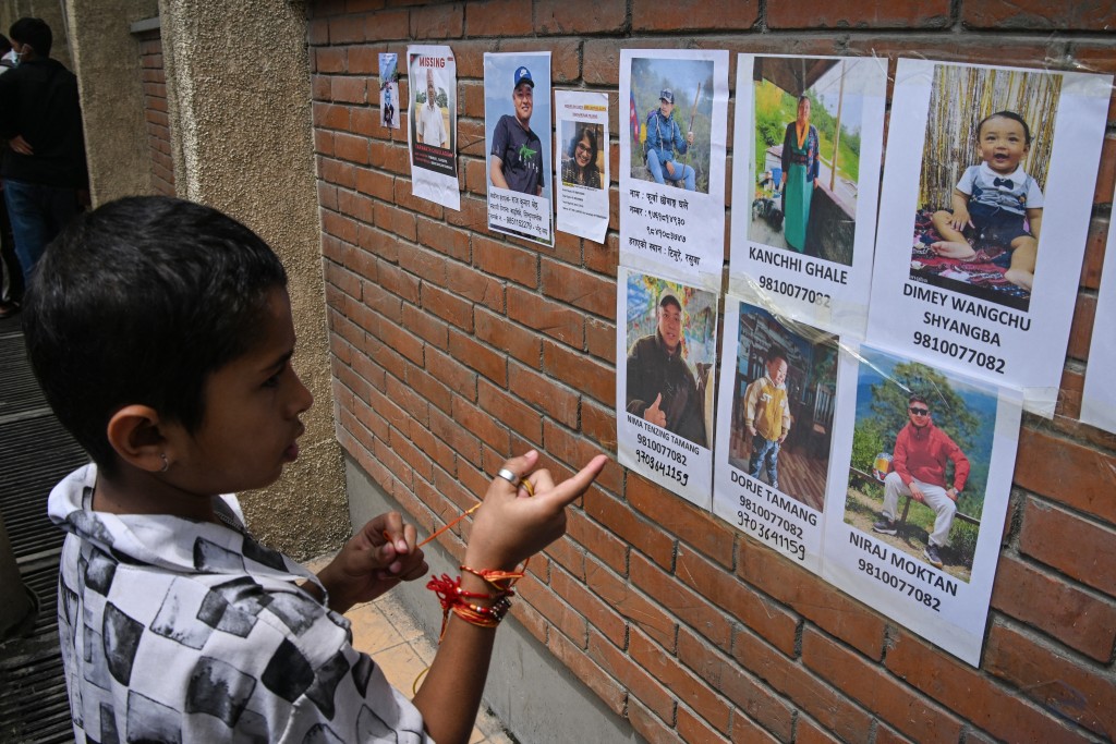 Photo by PRAKASH MATHEMA / AFP  A child looks at the photographs of missing people following flash floods, at a hospital in Kathmandu on August 28, 2026.