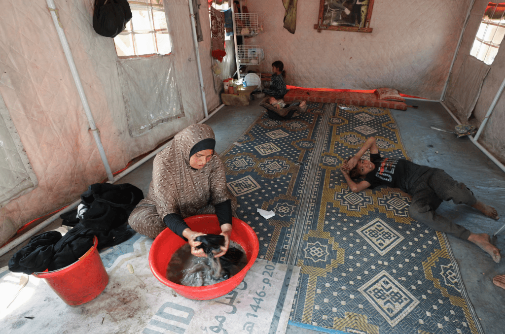 Palestinian woman, Mervat Hijazi, washes clothes inside the tent they took shelter after being displaced, in Gaza City, May 22, 2025. REUTERS/Mahmoud Issa