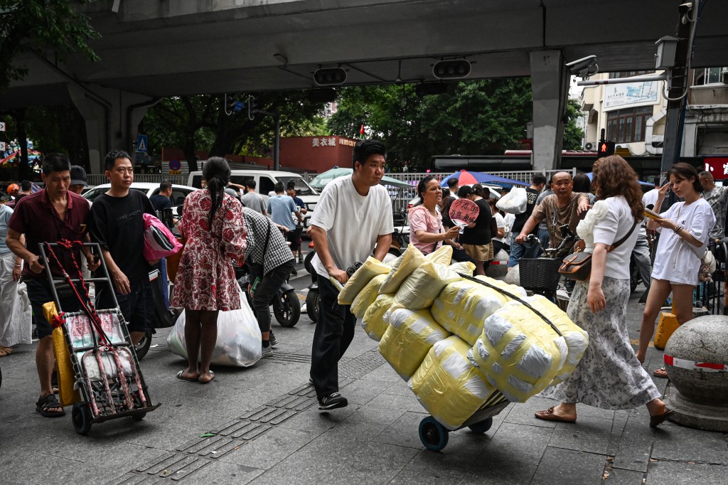 Photo by JADE GAO / AFP  The photo taken on April 16, 2026 shows a man wheeling bags of clothes toward a wholesale clothing market in Guangzhou, in southern China's Guangdong province.
